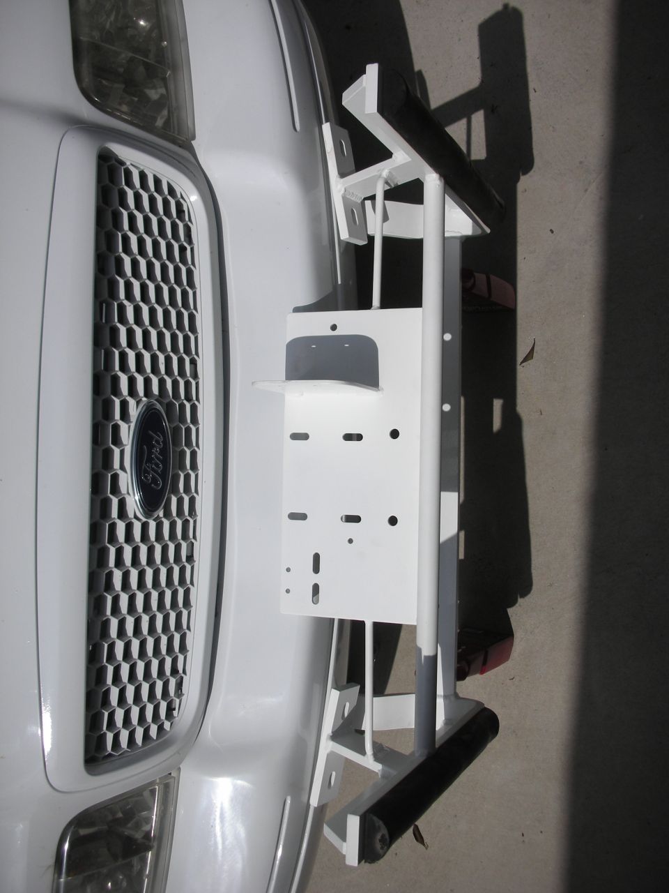 White push bumper with slotted mounting plate propped in front of a Ford grille