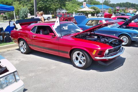 1980 Ford Mustang - A red 1970s Ford Mustang with racing stripes and a prominent rear spoiler is displayed with its hood open at a car show.