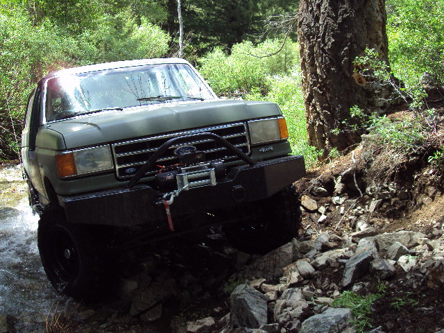 1989 Ford Bronco navigating rocky terrain and water crossing