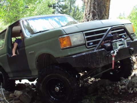 1989 Ford Bronco - A person is visible in the driver's seat of a lifted green Ford Bronco navigating a rocky trail.