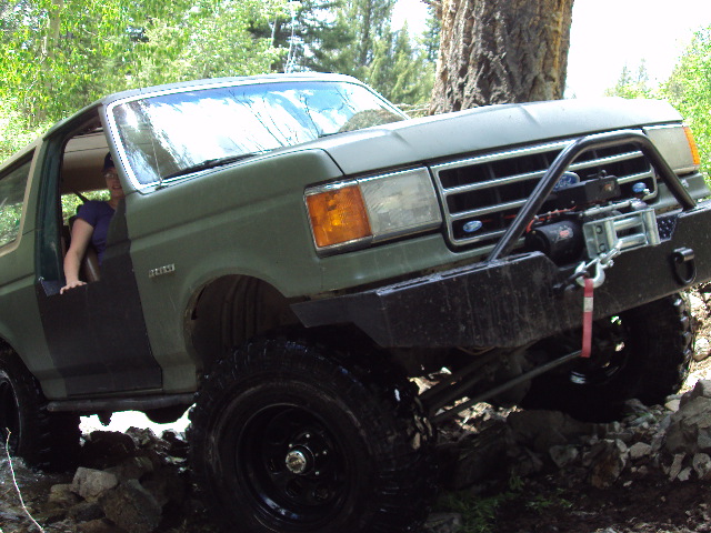 Green Ford Bronco with winch on front bumper driving over rocks
