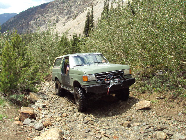 Green SUV with winch on rocky mountain trail. Looks like a 1987 Ford Bronco