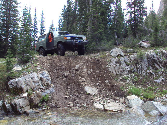 Green Ford Bronco climbing a dirt hill with the driver's door open