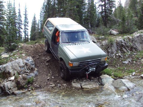 1989 Ford Bronco - Ford Bronco tackles a challenging off-road obstacle with water and rocks.