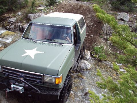 1989 Ford Bronco - This 1989 Ford Bronco is navigating a challenging off-road trail with water and rocks.
