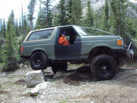 1989 Ford Bronco - A person in an orange shirt drives a lifted 1989 Ford Bronco over rocks on a trail.