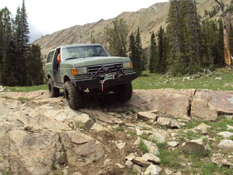 1989 Ford Bronco - Green 1989 Ford Bronco tackling a challenging rocky off-road path in a mountainous area.