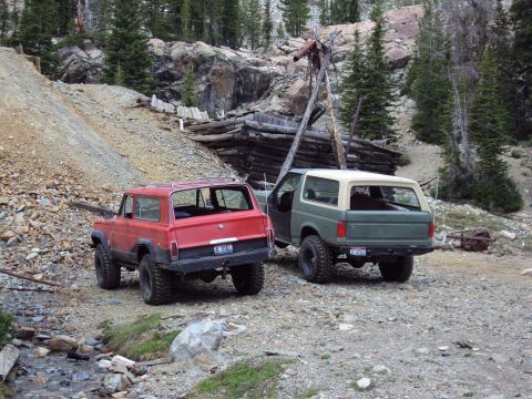 1989 Ford Bronco - Two SUVs, a green 1987 Ford Bronco and a red Jeep Cherokee, are parked near an abandoned mine in a mountainous, wooded area.
