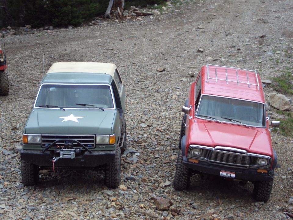 Green SUV with a white star on the hood and a winch, next to a red SUV with a roof rack
