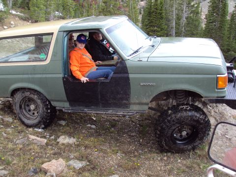 1989 Ford Bronco - This 1989 Ford Bronco, seen in a rocky, wooded area, features off-road tires and a two-tone green and tan paint scheme.