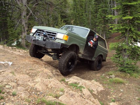 1989 Ford Bronco - A green Ford Bronco navigates a steep, rocky trail in a wooded area.