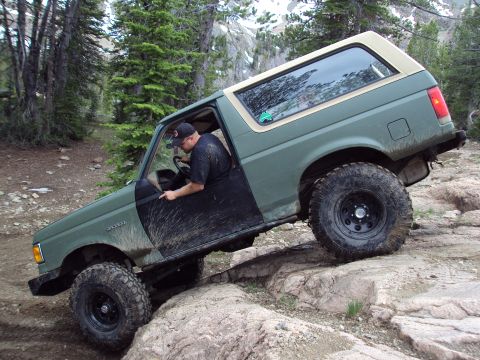 1989 Ford Bronco - Driver maneuvers a 1989 Ford Bronco over a challenging rock obstacle on a trail.