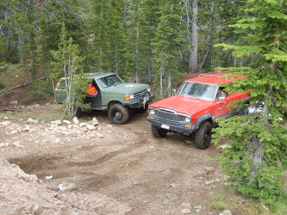 Green off-road SUV with a star emblem on the hood and a red SUV with a roof rack on a dirt trail