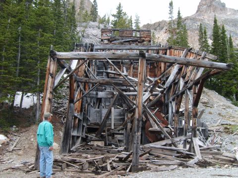 1989 Ford Bronco - A person surveys the ruins of an old wooden mine structure in a mountainous, wooded area.