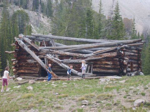 1989 Ford Bronco - Children explore a decaying log cabin in a remote mountain landscape.