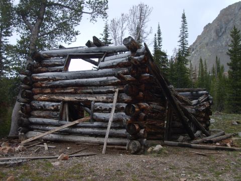 1989 Ford Bronco - An old, decaying log cabin sits in a remote mountain landscape, with a watermark for Supermotors.net visible.