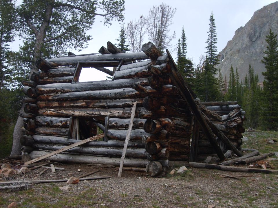 Dilapidated log cabin in mountainous woods with Supermotors.net watermark
