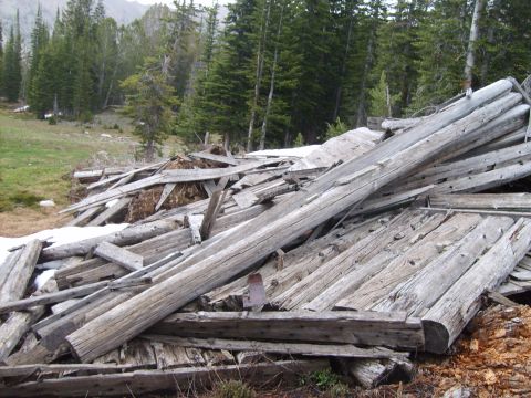 1989 Ford Bronco - A large pile of decaying wooden planks and logs lies scattered in a mountainous, forested landscape.