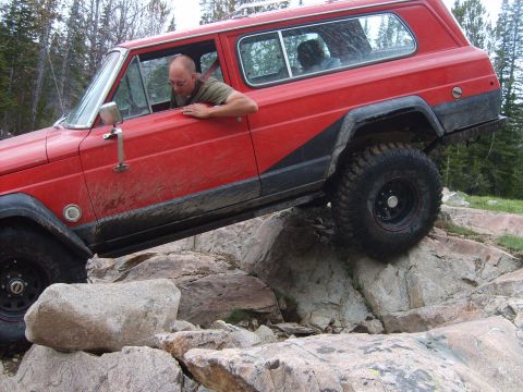 1989 Ford Bronco - A red Jeep Cherokee Chief navigates a rocky trail, demonstrating its off-road capabilities.
