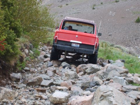 1989 Ford Bronco - This red SUV navigates a challenging rocky terrain on a mountain trail.
