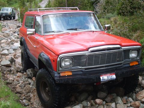 1989 Ford Bronco - A red Jeep Wagoneer navigates a rocky off-road path with another vehicle following behind.