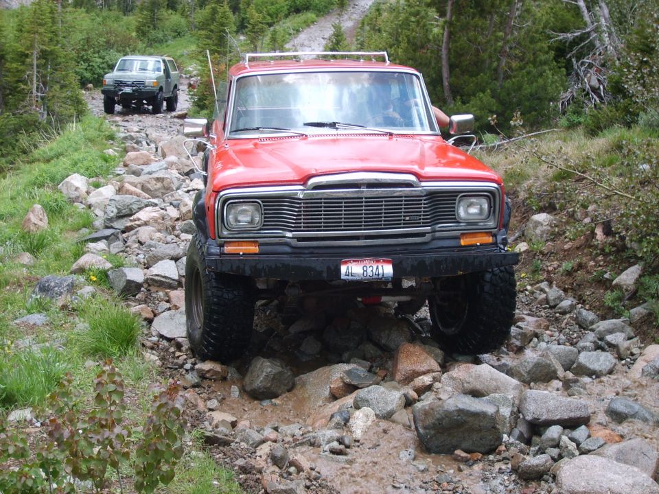 Red Jeep Wagoneer with off-road tires navigating a rocky trail, front view