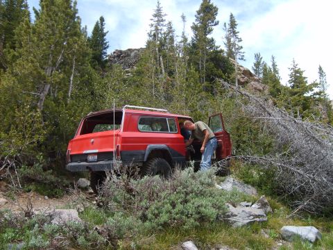 1989 Ford Bronco - A red SUV is parked off-road in a wooded area with a person attending to the interior.