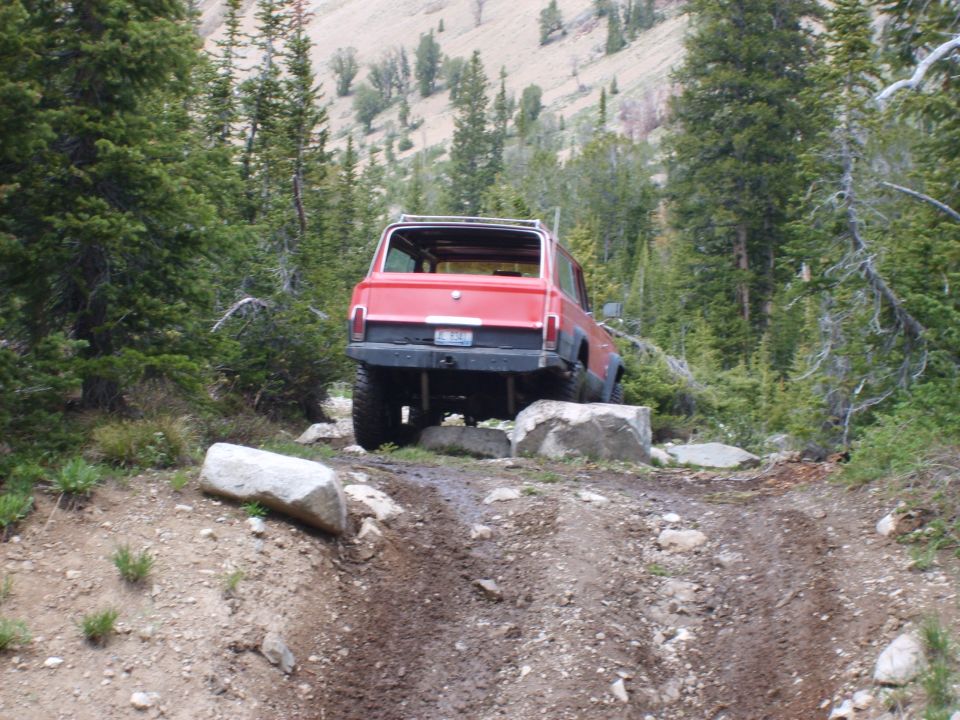 Red SUV with a black bumper navigating rocks on a dirt trail in a forest