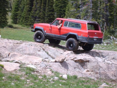 1989 Ford Bronco - A red Jeep Cherokee XJ navigates a rocky trail with a driver visible inside.