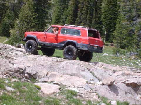 1989 Ford Bronco - This red Jeep Cherokee Chief is navigating a rocky trail with a driver inside.
