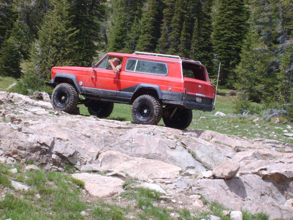 Red Jeep Cherokee Chief off-roading on rocks with trees in background