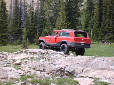 1989 Ford Bronco - A red Jeep Cherokee XJ navigates a rocky trail in a wooded area.