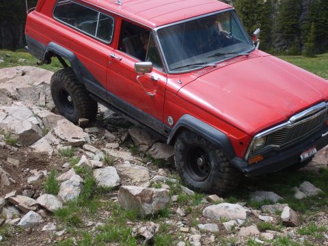 1989 Ford Bronco - This red Jeep Cherokee Chief is shown off-roading over a rocky path.