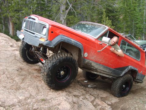 1989 Ford Bronco - This red Jeep Cherokee is navigating a rocky trail with a driver looking out the window.