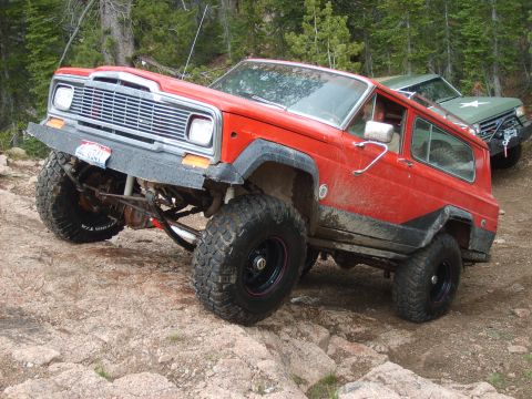 1989 Ford Bronco - A red Jeep Cherokee Chief navigates a rocky trail, with another off-road vehicle visible behind it.