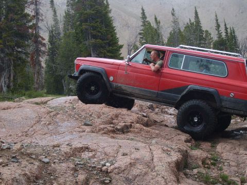 1989 Ford Bronco - A red Jeep Cherokee navigates a rocky trail with one wheel lifted off the ground.