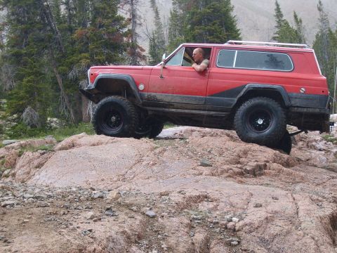 1989 Ford Bronco - A red SUV navigates a rocky trail in a mountainous, wooded area.