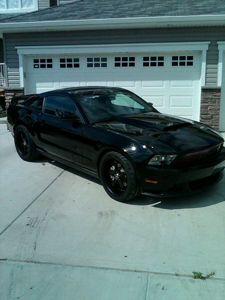 2011 Ford Mustang - A black 2011 Ford Mustang is shown from a three-quarter front view, parked in front of a garage.