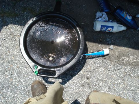 1988 Ford Bronco - A used oil drain pan sits on the ground next to a tube of sealant and some automotive fluid bottles.