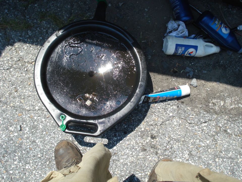 Oil drain pan filled with used oil, next to a tube of sealant and some bottles