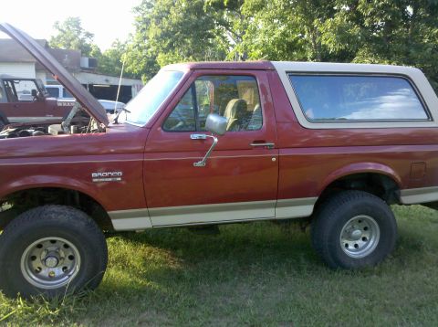 1988 Ford Bronco - A red Ford Bronco with a tan top is parked on grass, with its hood open.