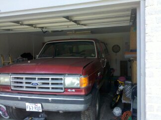 1988 Ford Bronco - A red Ford Bronco is parked inside a garage, showing its front grille and headlights.