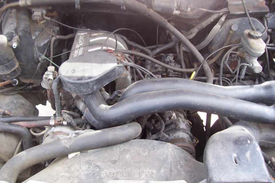 Engine bay of a 1987 Ford Bronco, showing hoses, engine block, and other components