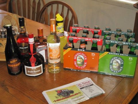 1990 Ford Bronco - A collection of alcoholic beverages, including various liquor bottles and cases of Woodchuck Draft Cider, are displayed on a wooden table.