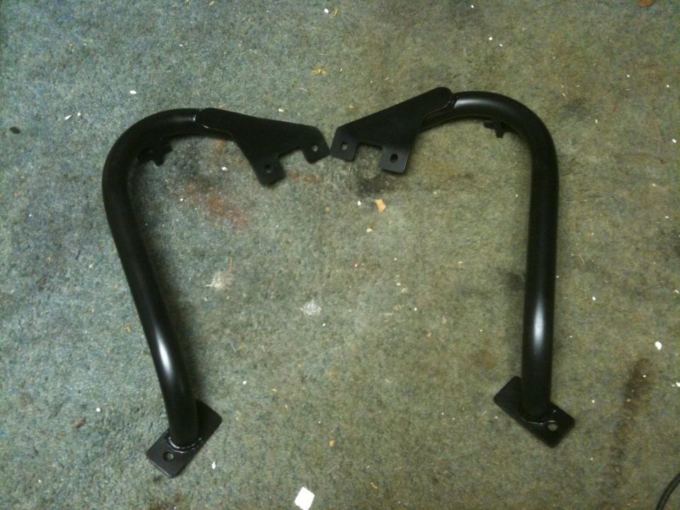 Two black metal tube steps with mounting brackets, lying on a carpeted floor