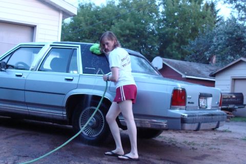 2000 Mercury Grand Marquis - Woman washes a light blue sedan, likely a Ford Crown Victoria or Mercury Grand Marquis, on a driveway.