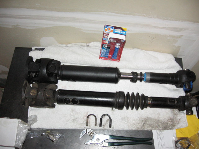 Two driveshafts with U-joints on a towel, plus Permatex thread locker box and pliers