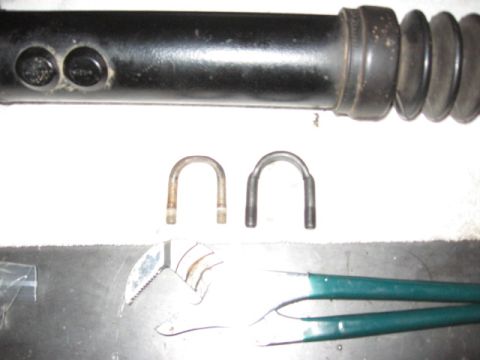 1995 Ford Bronco - A collection of automotive parts, including a shock absorber, U-bolts, and pliers, are laid out on a flat surface.
