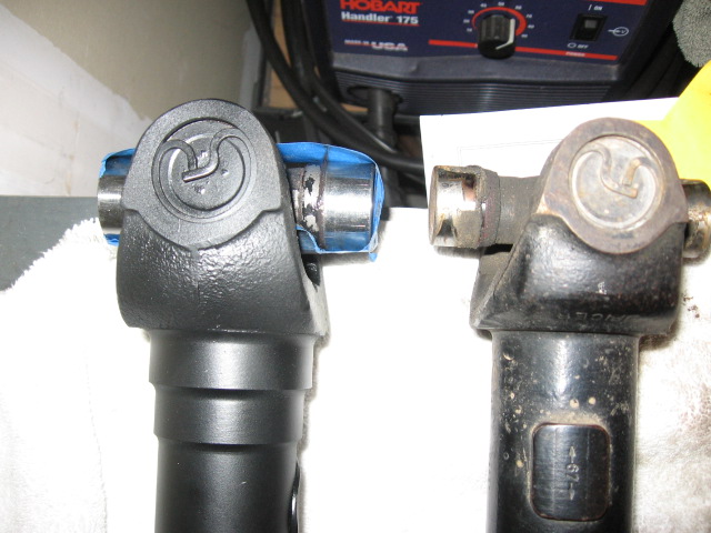 New black and old worn driveshaft yokes with U-joints on a towel by a Hobart welder