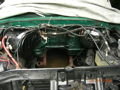 1979 Ford F-100 - The engine bay of a green vehicle is shown, with various hoses and wiring present. A tarp covers the upper portion.